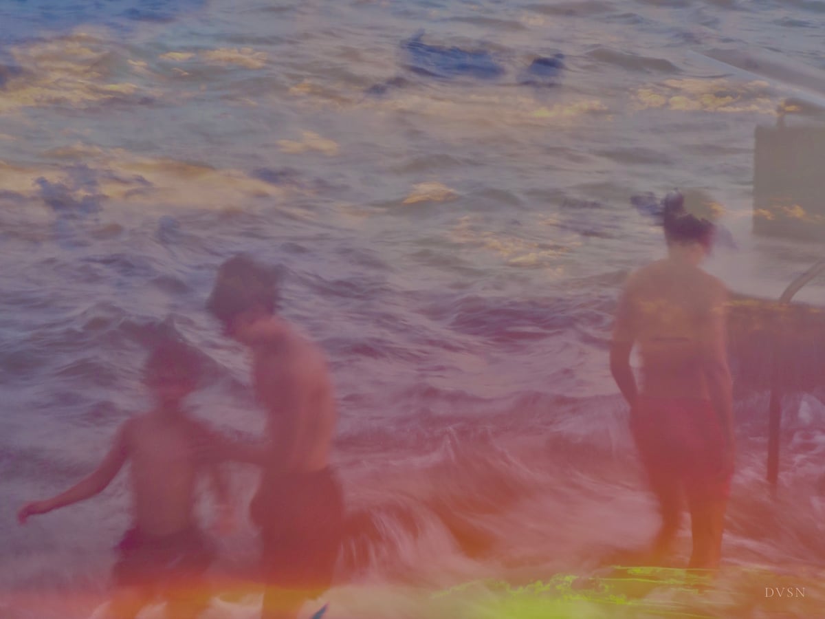 Blurred bathers in rough waves under pastel evening light.