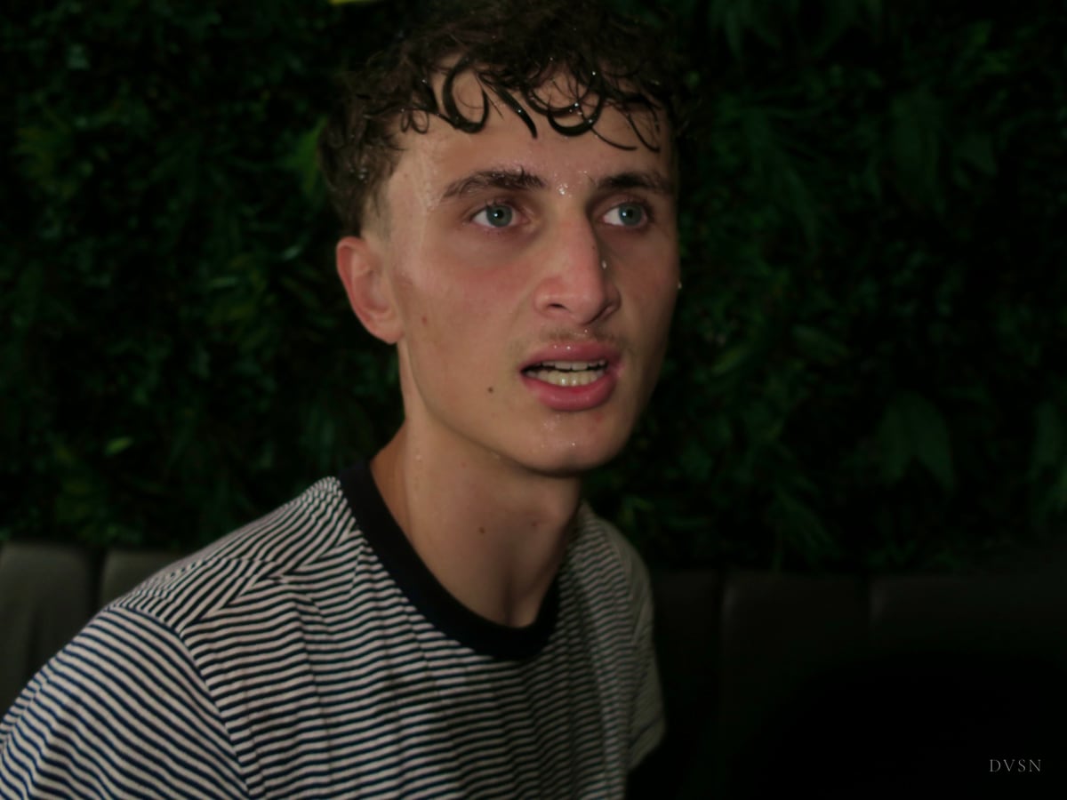 Close portrait of a young man with wet curls and a striped T-shirt, lit by flash against dark leaves.