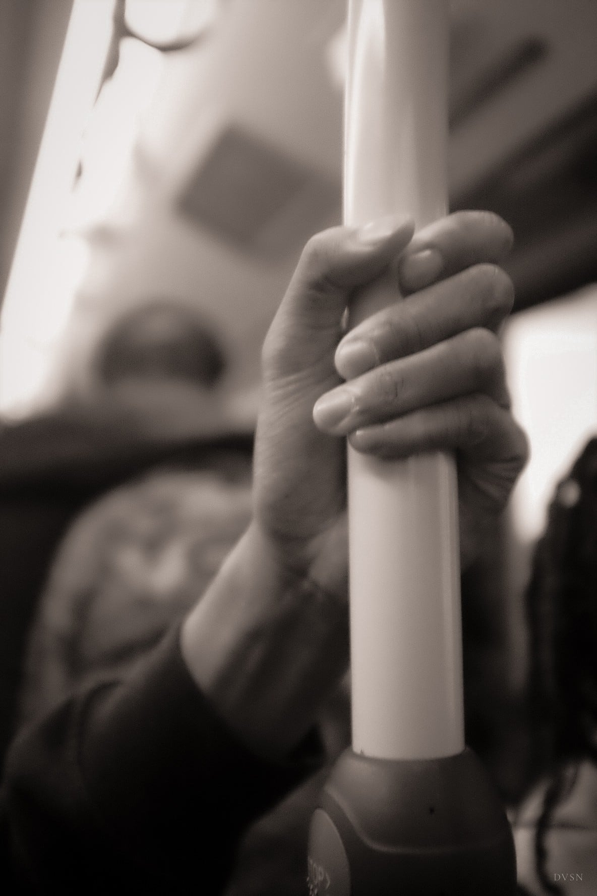 A hand gripping a pole on a bus, in sepia tones.