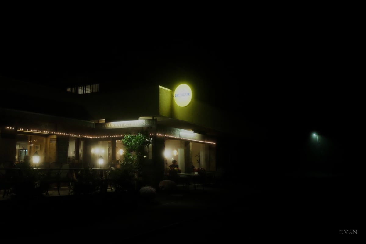 A restaurant glowing in the foggy night, surrounded by darkness.