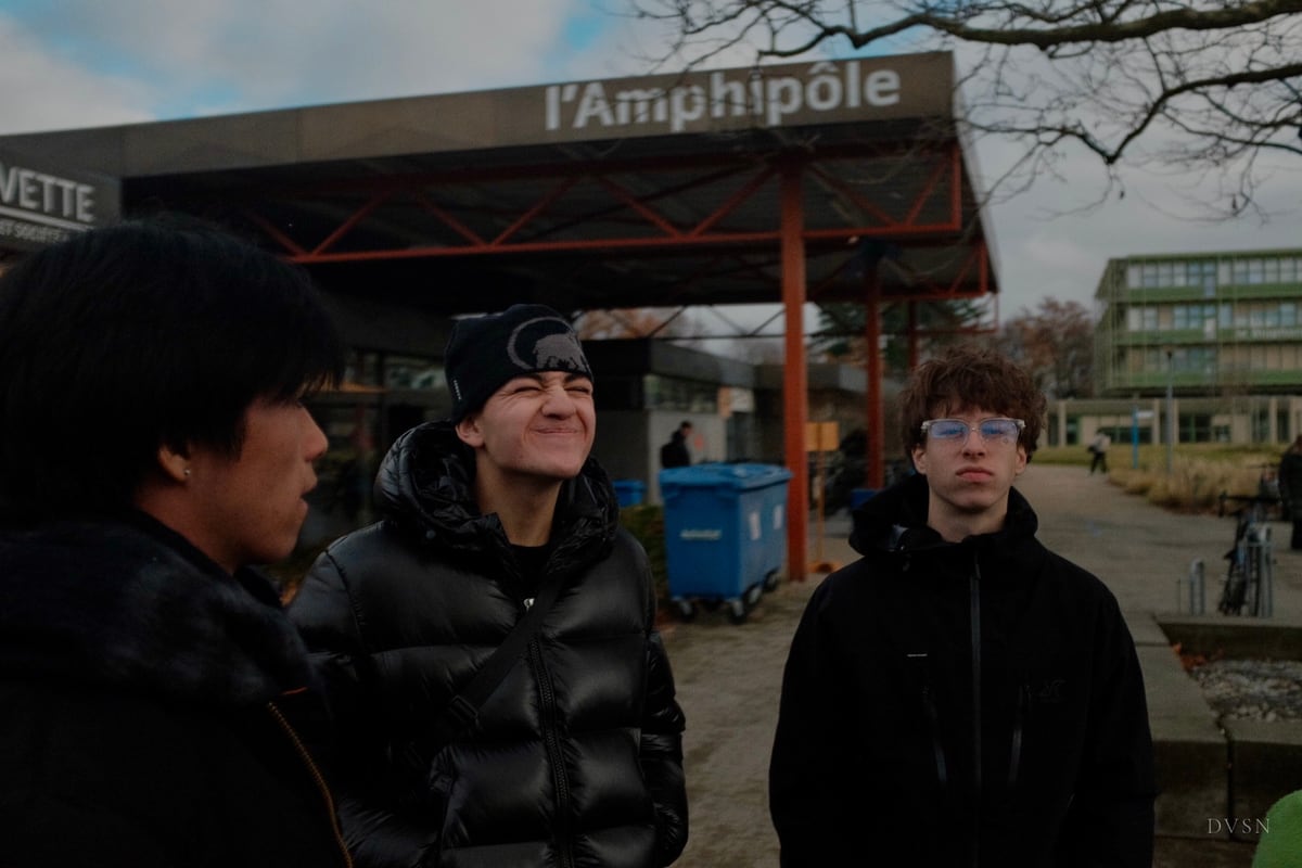 Three young people outside a building on an overcast day; one squints with a grin.
