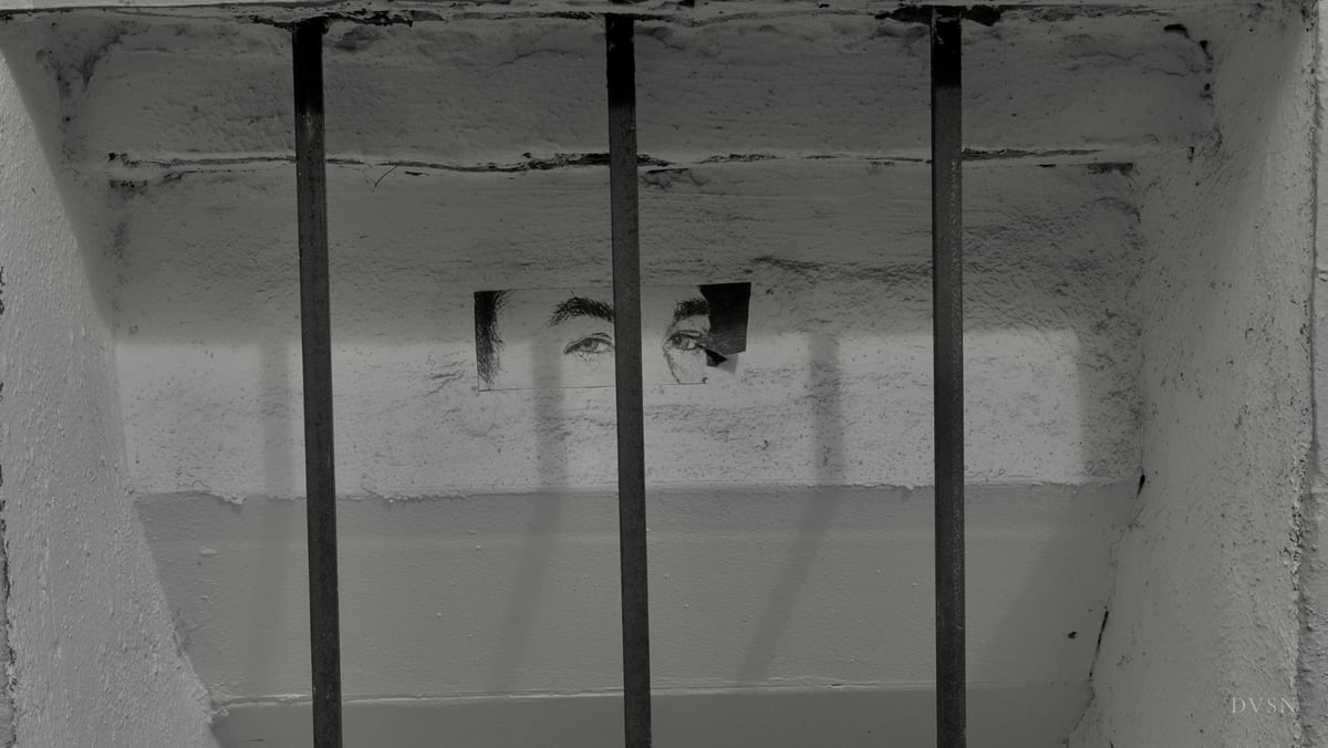 A printed pair of eyes pasted on a wall behind window bars.