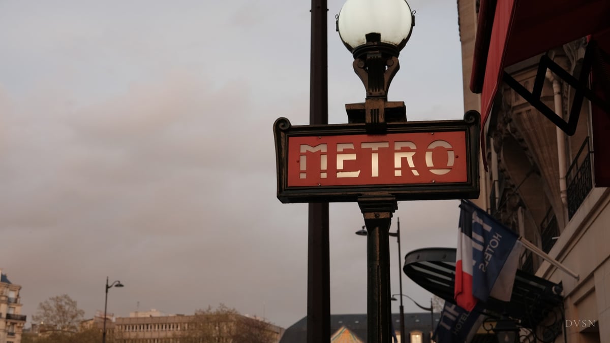 A red Metro sign beneath a globe streetlamp at dusk.