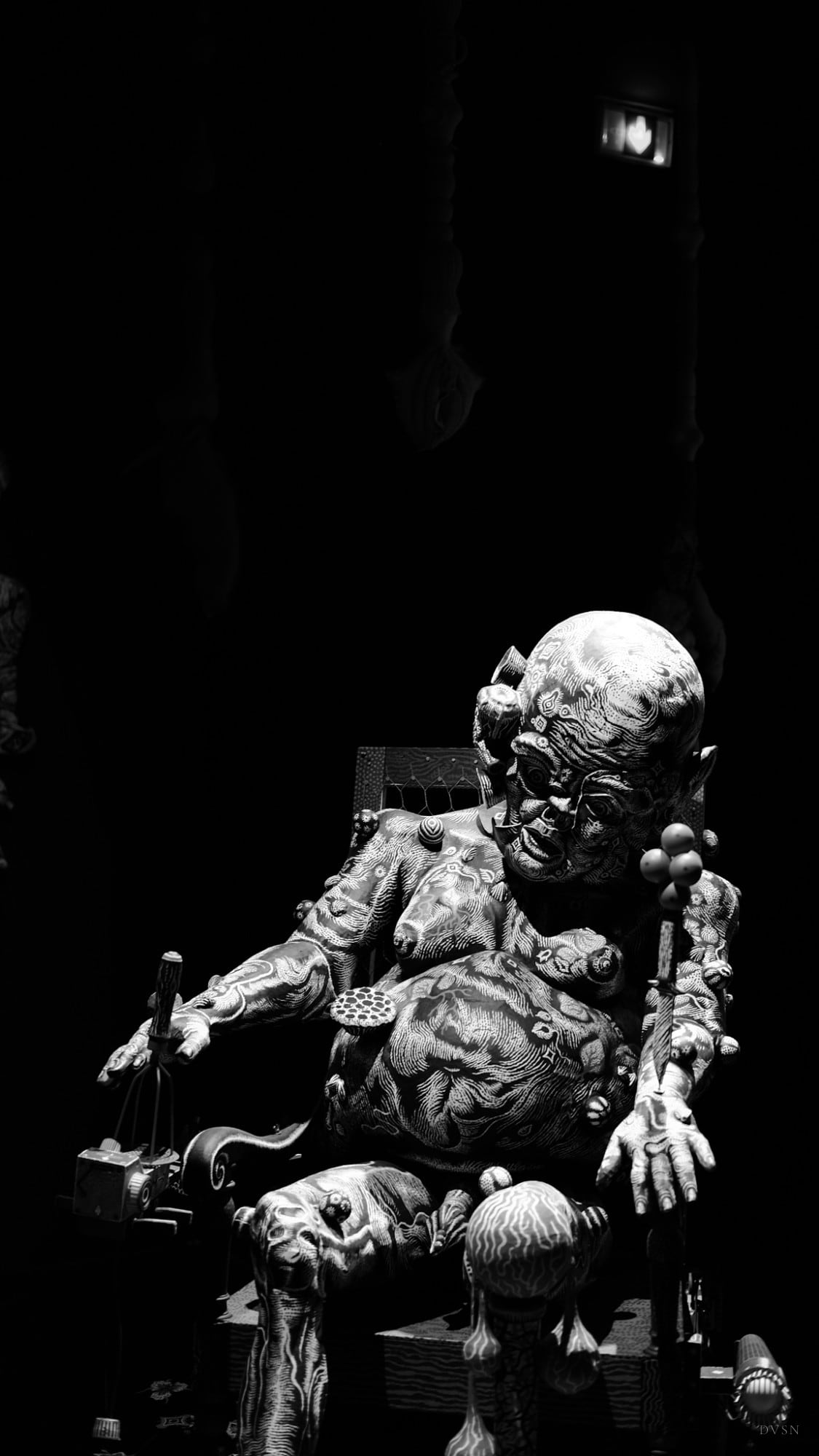 A patterned sculpture of a seated figure emerging from darkness.